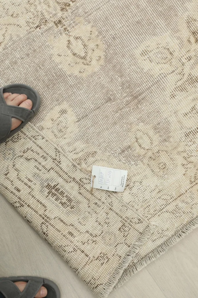 Foot resting on the rug, showing scale and the low pile texture, with a product tag visible