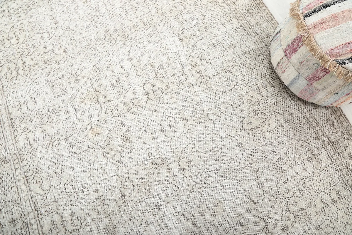 Detailed view of the rug's low pile and faded floral motifs, with an ottoman in the corner
