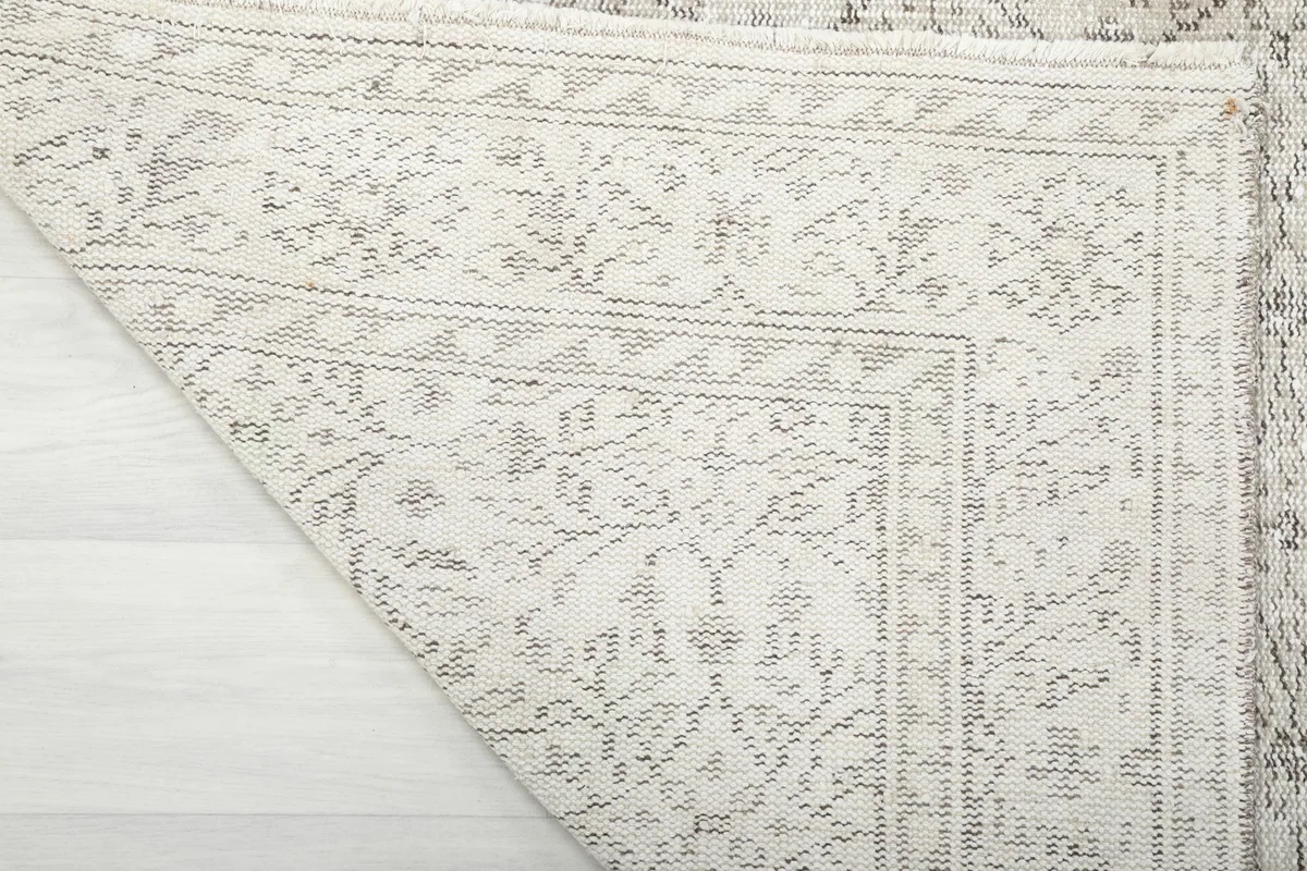 Corner of the rug folded back, revealing the reverse side and the tightly woven cotton foundation