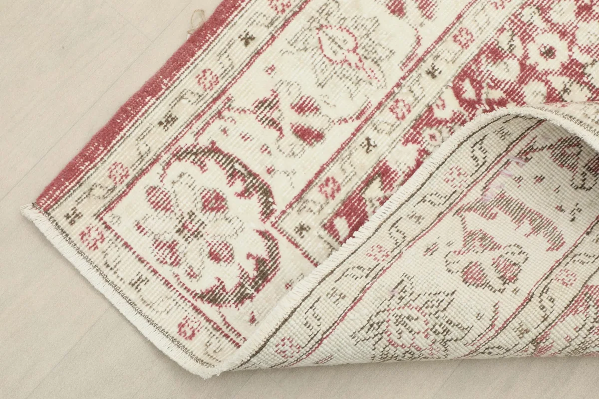 Corner of the rose and ivory rug folded back, showing the cotton foundation and reverse side