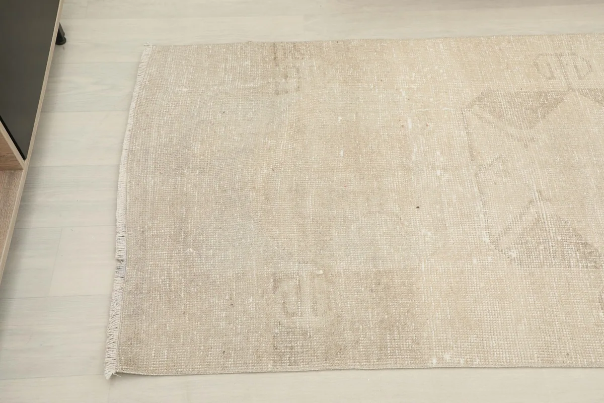 Angled view of the other end of the beige runner rug, showing its natural vintage patina
