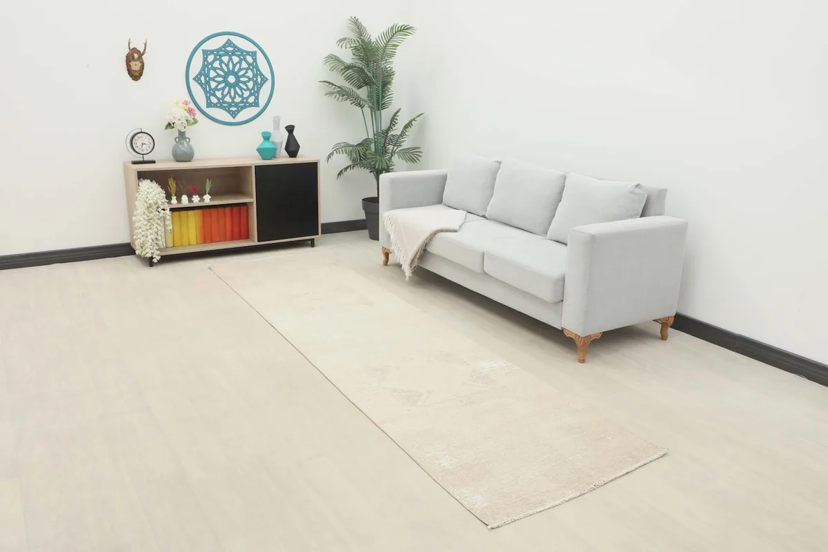 Beige vintage runner rug laid out in a modern room with a light gray sofa and wooden floor