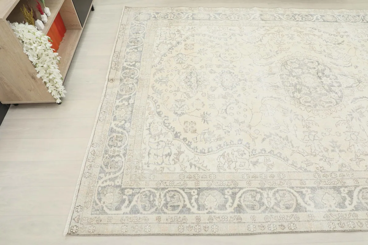Corner view of the vintage rug, showing the faded gray patterns and ivory background