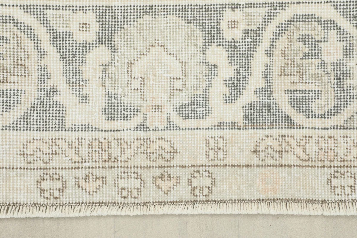 Detailed shot of the rug's border, featuring intricate gray and ivory patterns and short fringes