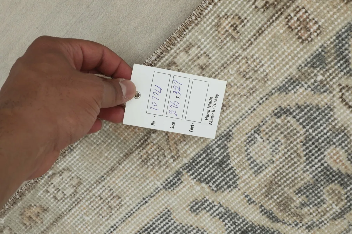 Hand holding a tag showing the rug's size and origin, with the back of the rug visible