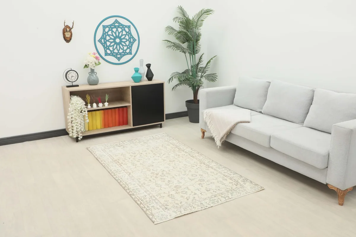Ivory floral rug placed in a living room setting with a light gray couch and wooden cabinet