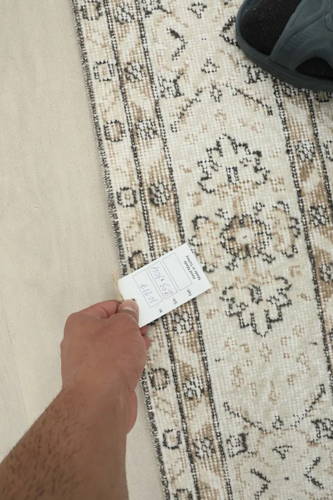 Hand holding a size tag next to the rug, offering a sense of scale and texture.
