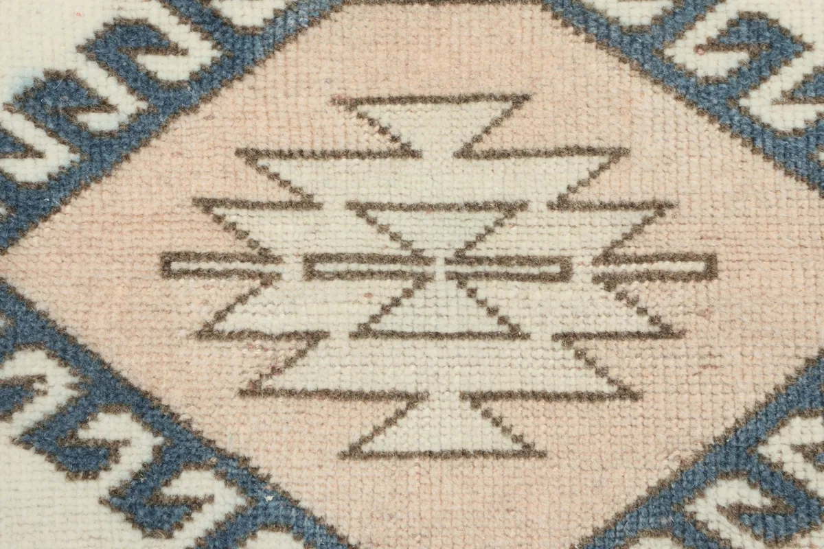 Close-up of a central pink diamond motif with ivory and blue geometric details, revealing the knotting.