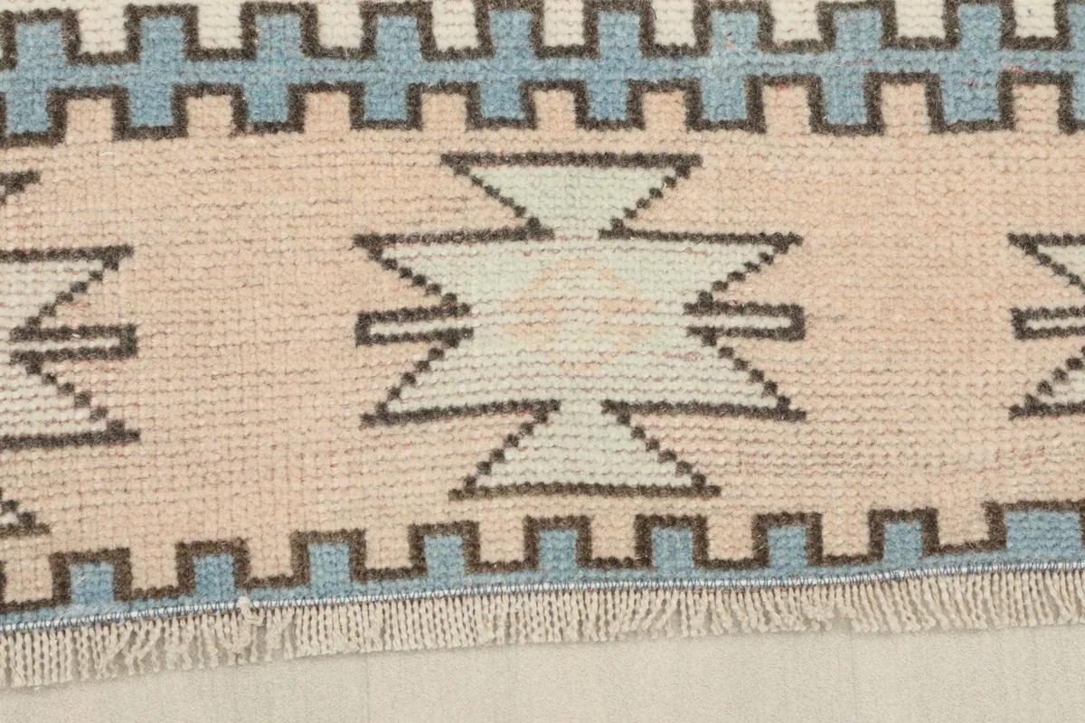 Close-up of the rug's border, displaying the pink and blue serrated edge patterns and short fringe.