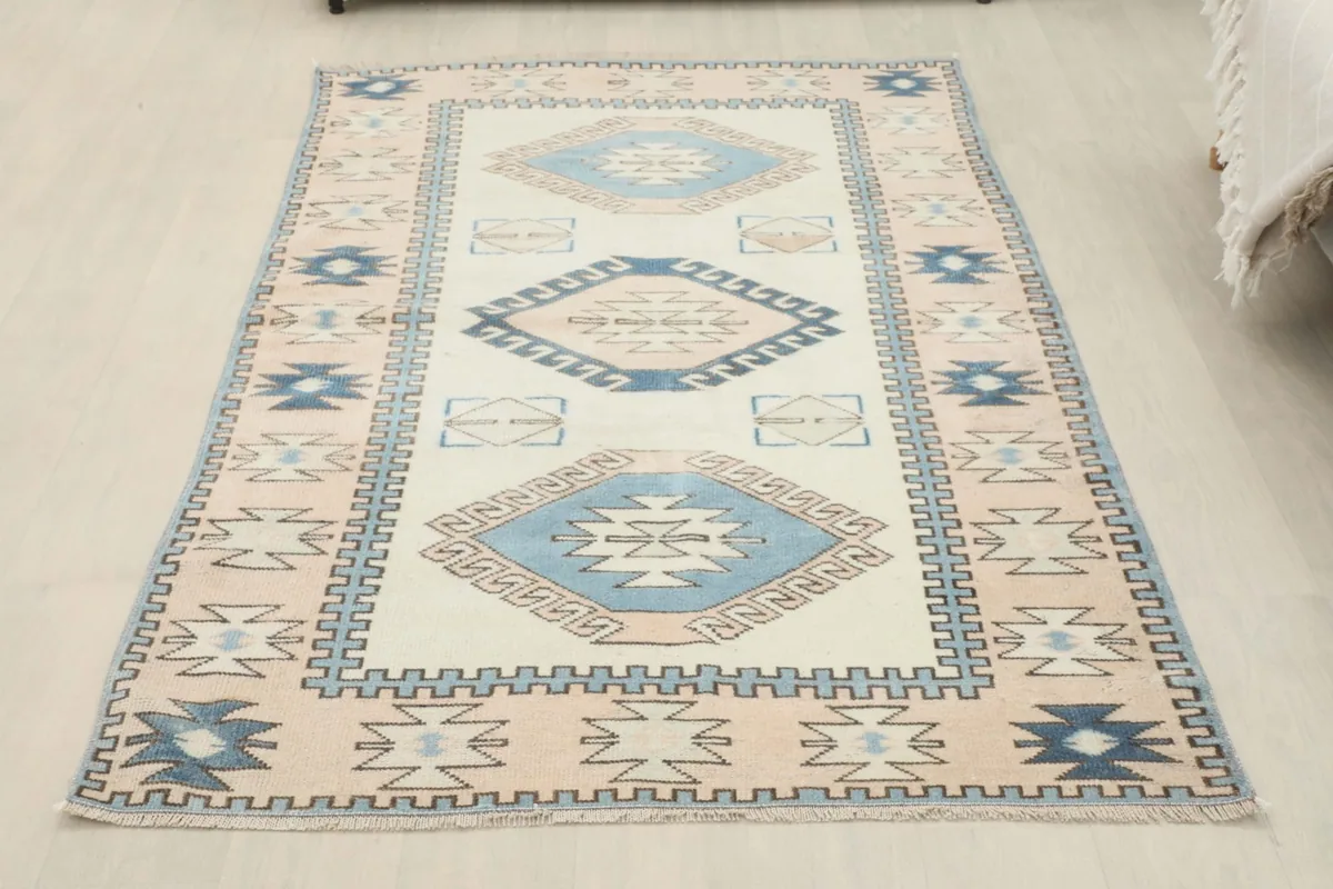 Full overhead view of the vintage Anatolian rug, clearly showing all the ivory, blue, and pink tribal patterns.
