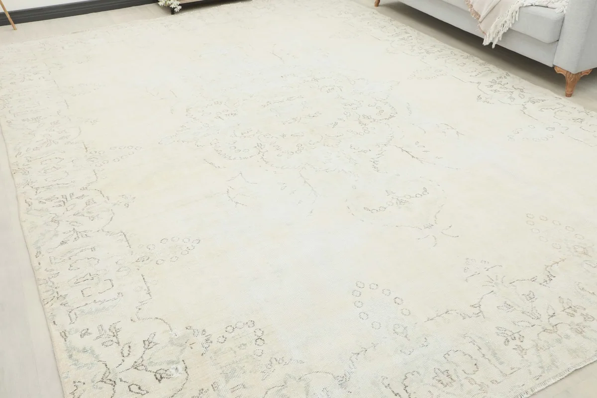 Angled view of the cream rug on the floor, highlighting the subtle faded floral patterns.