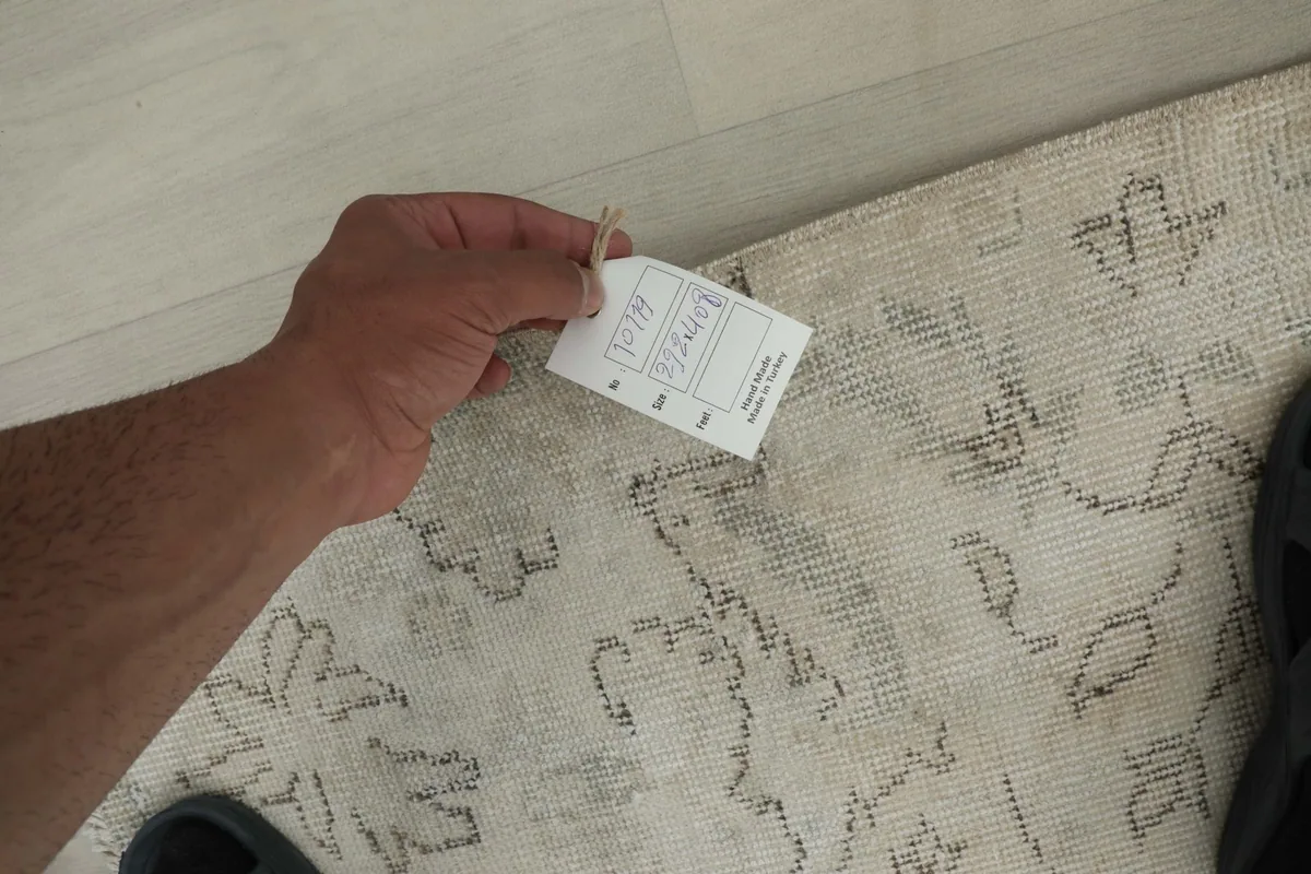 Hand holding a product tag near the rug, showing texture and general condition up close.