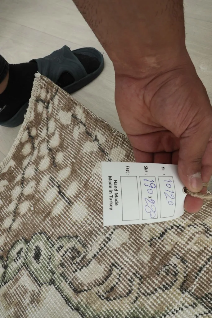 Hand holding a tag on the back of the rug, showing details of its hand-made origin in Turkey.