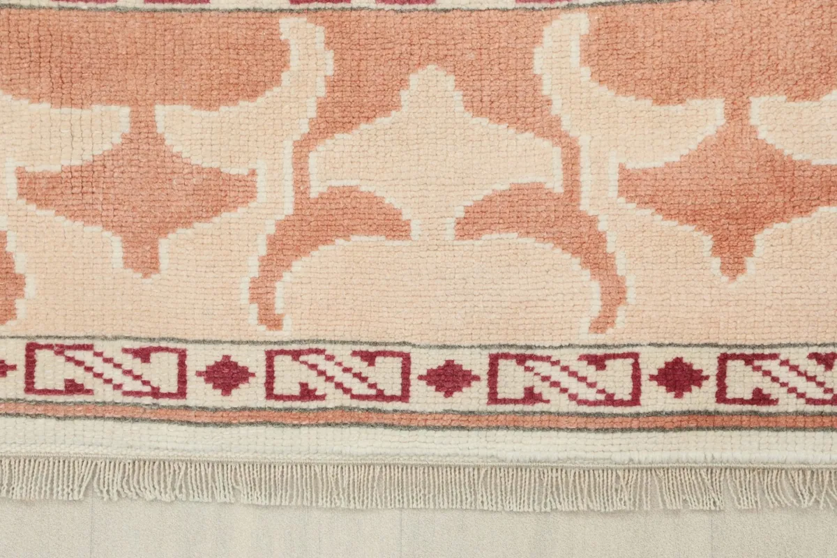 Close-up of the rose border pattern and fringe detail of the hand-knotted rug
