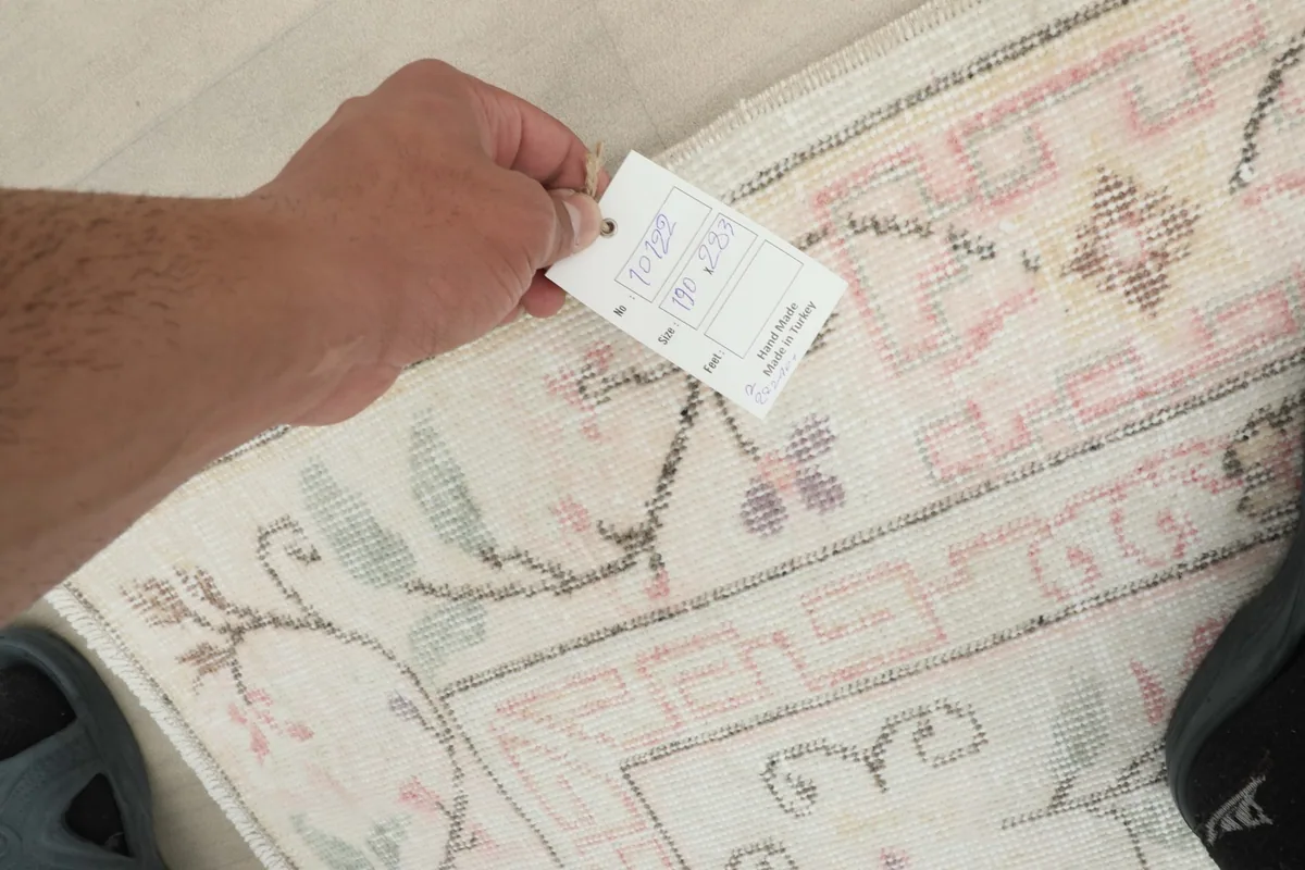 Hand holding a tag over the back of the rug, showing the knots and cotton foundation.