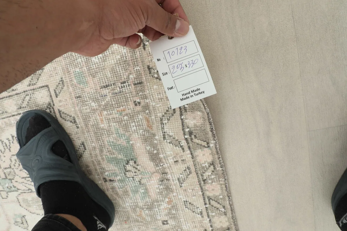 Hand holding a tag showing rug dimensions and 'Hand Made in Turkey'