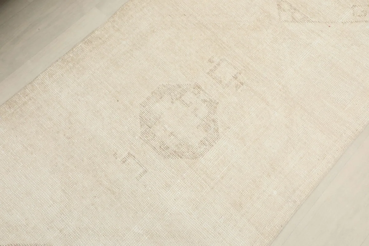 Detailed view of a central, faint geometric medallion motif on the ivory rug's field.