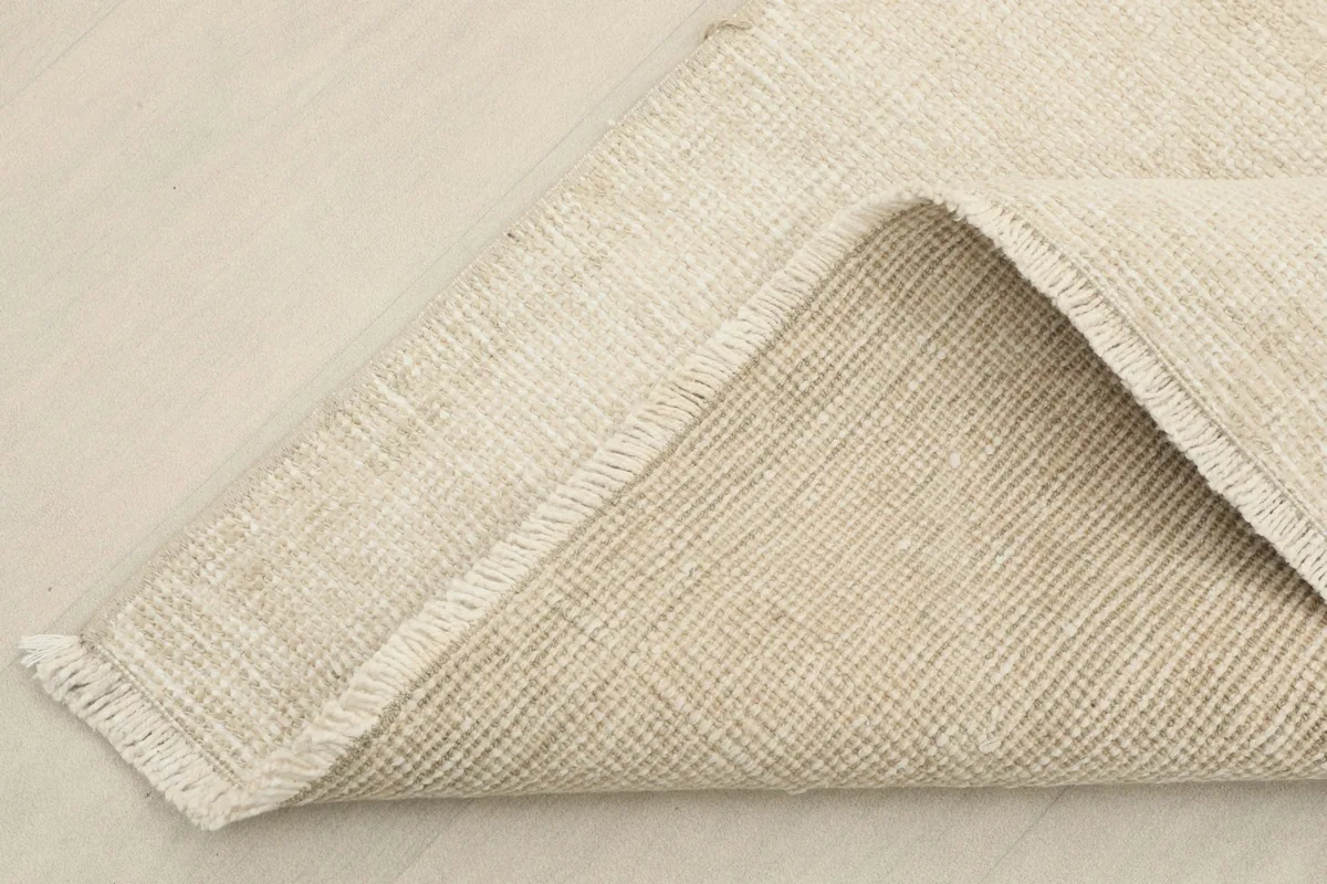 Corner of the rug folded back to show the hand-knotted wool pile on a cotton foundation.