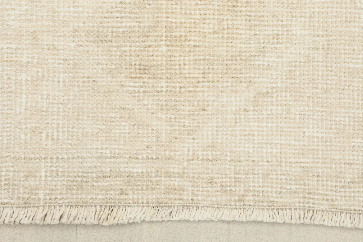 Close-up of the short, natural cotton fringe and the low wool pile texture of the rug's edge.