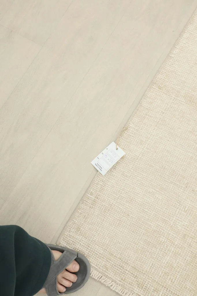 A foot wearing a slipper next to the ivory runner rug, with a product tag visible on the floor.