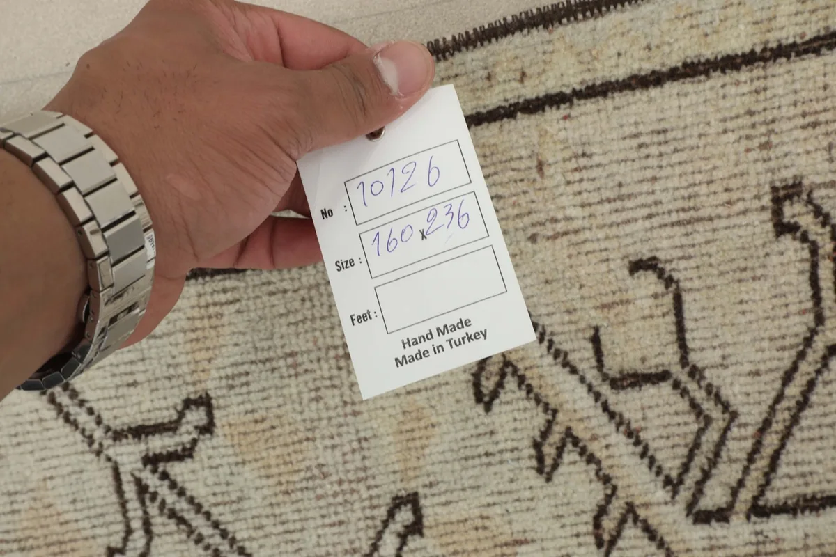 Hand holding a tag showing the rug's dimensions and 'Hand Made in Turkey' label