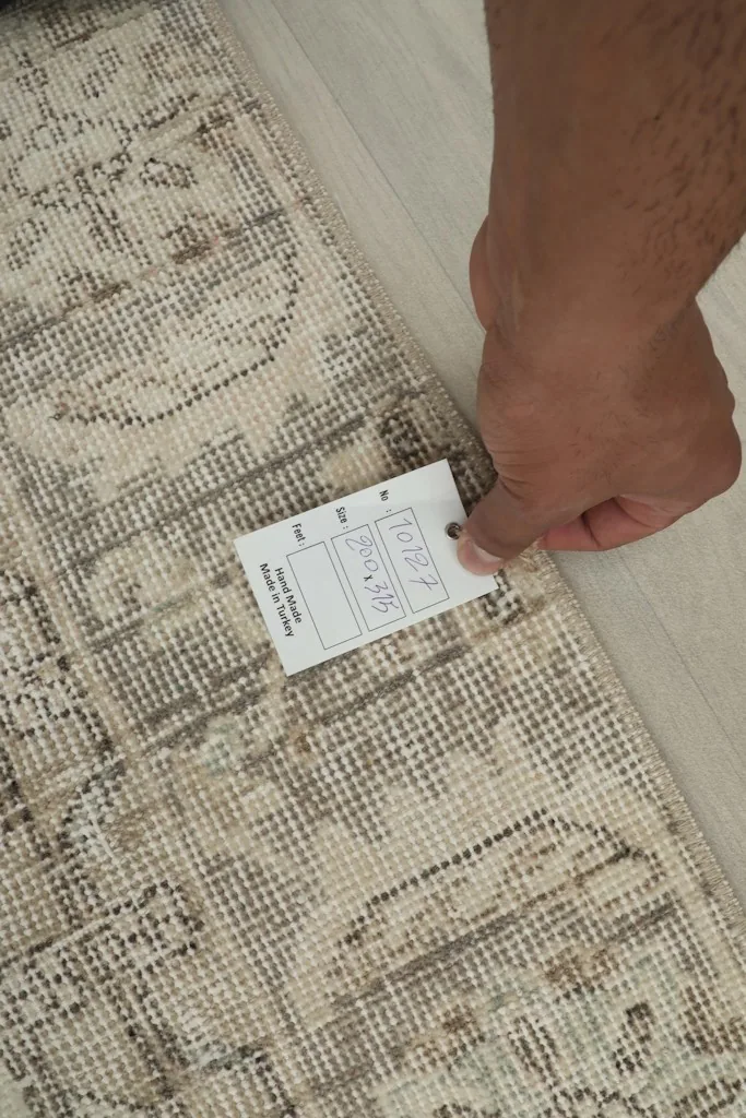 Hand holding a tag, showing the low wool pile and the texture of the vintage Anatolian rug