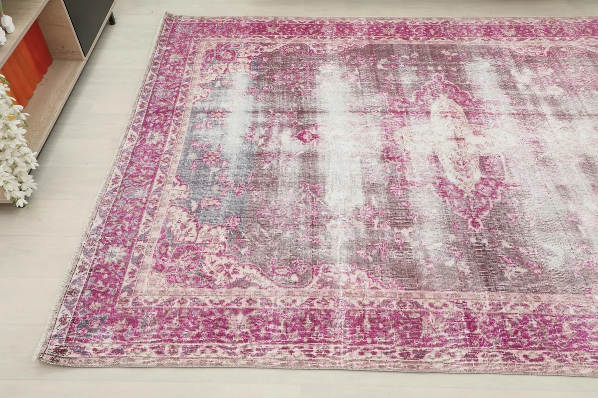 Angled view of the vintage rug, highlighting the faded pink border and gray field