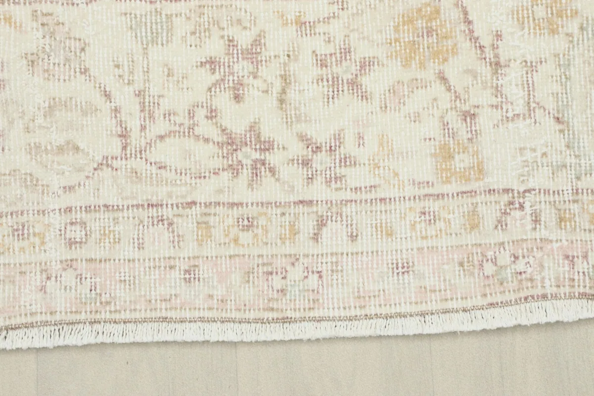Close-up of the rug's border, showcasing the intricate floral and geometric motifs in beige and rose
