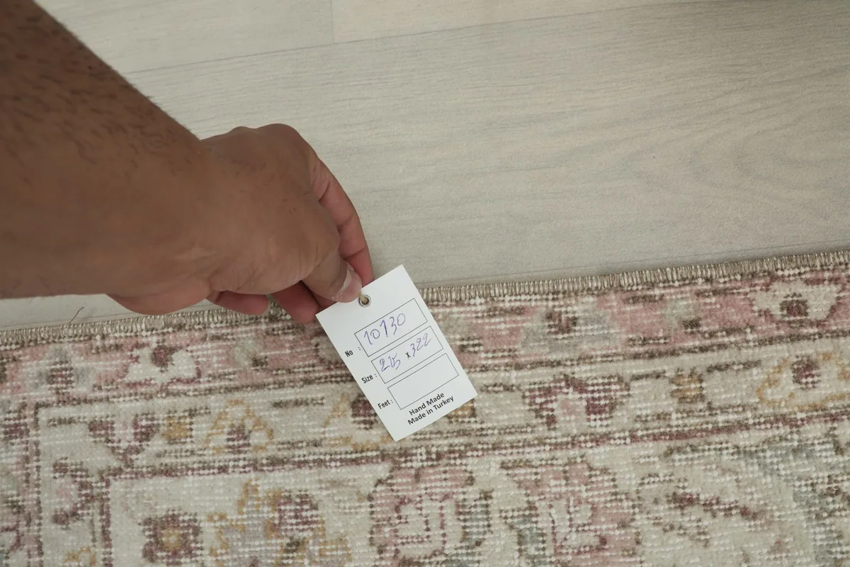 Hand holding a tag showing the rug's details, including its origin and size, against the rug's edge