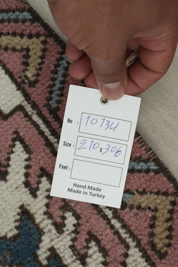 Hand holding a tag showing the rug's dimensions and origin