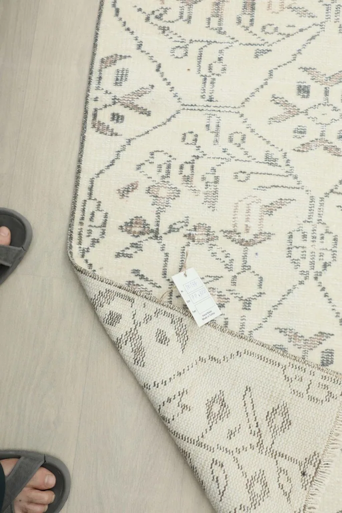 Top-down view of the rug's corner with a tag and a person's feet, showing scale