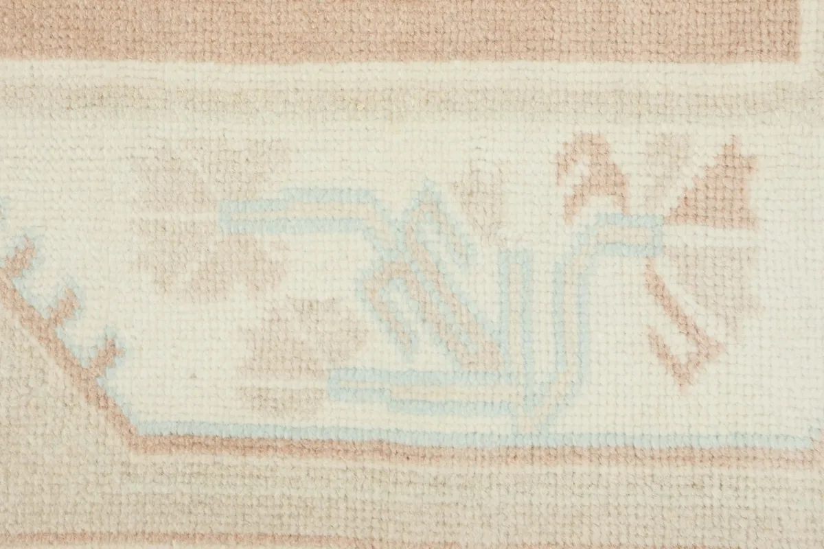 Detailed view of the hand-knotted wool pile and intricate geometric motifs in blue and rose tones.