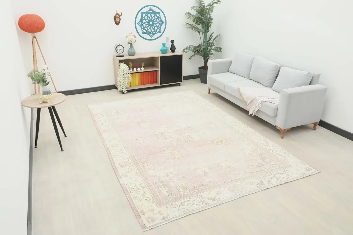 Large rose vintage area rug laid out in a living room setting with a light-colored sofa.