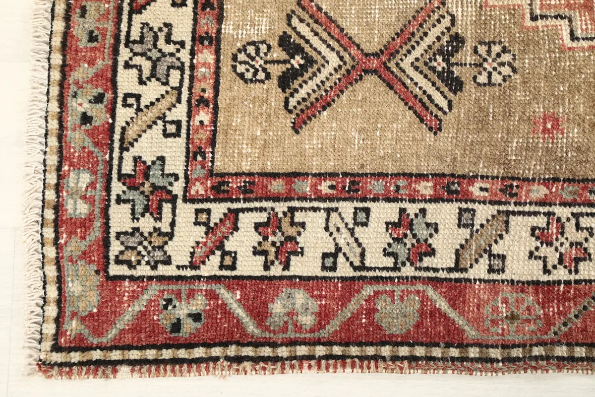 Corner detail of the rug, illustrating the red border with ivory and black accents and the fringe.