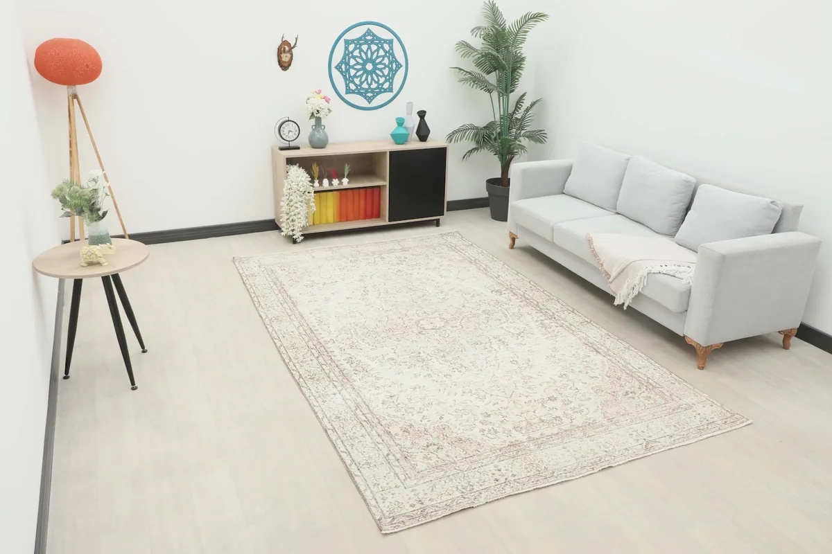 Vintage ivory and rose rug displayed in a living room setting with a sofa and side table.