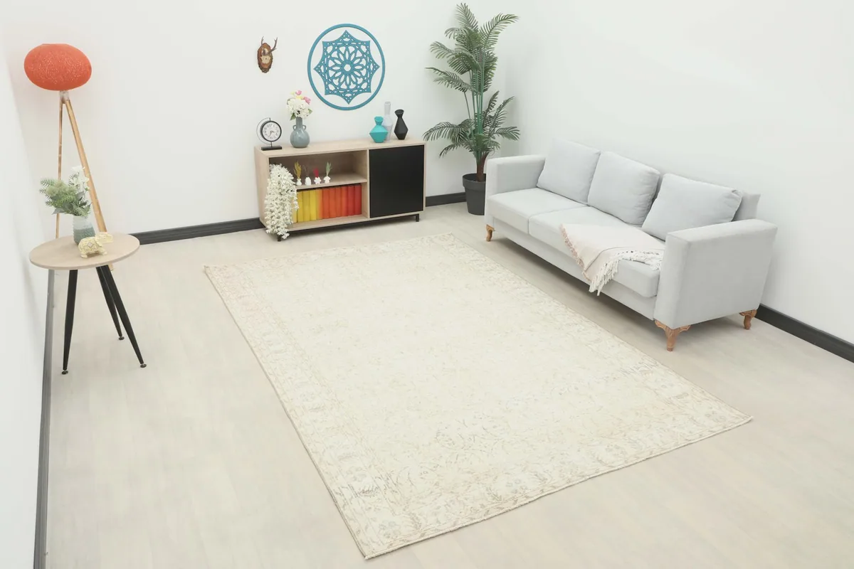 Large cream and beige vintage rug displayed in a modern living room setting with a light gray sofa