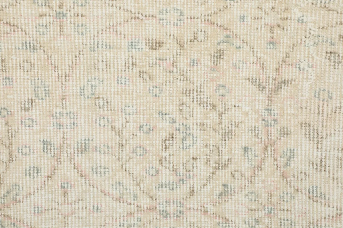 Macro shot of the low wool pile and hand-knotted texture, revealing faded cream, beige, and blue threads
