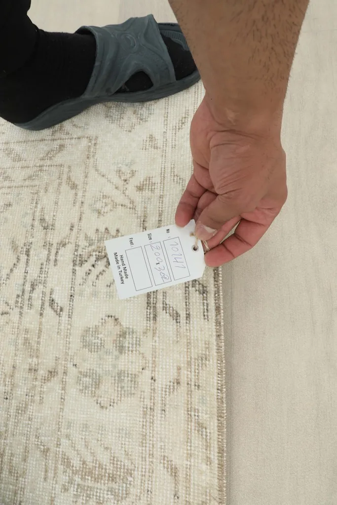 Hand holding a tag next to the rug's border, indicating its size and vintage nature