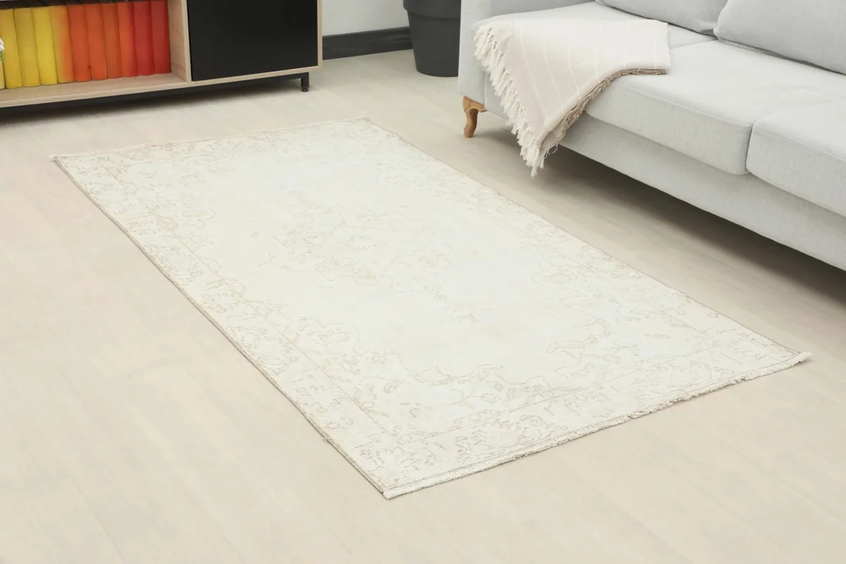 Angle view of the ivory beige rug placed in a living room, showing its subtle pattern and texture.