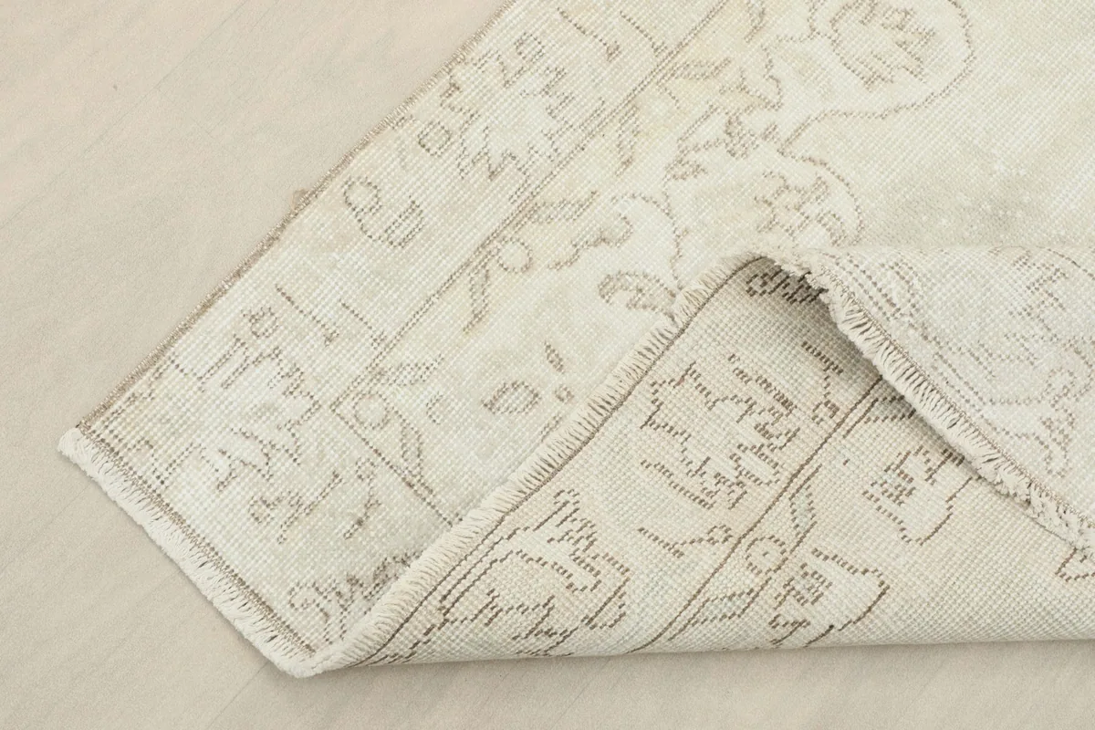 Corner of the ivory beige rug folded back, showing the back of the hand-knotted cotton foundation.