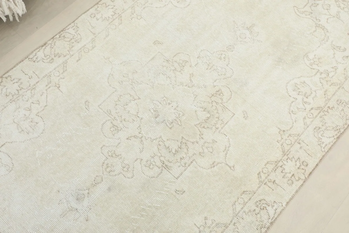 Overhead view focusing on the central medallion and faded geometric patterns of the ivory beige rug.