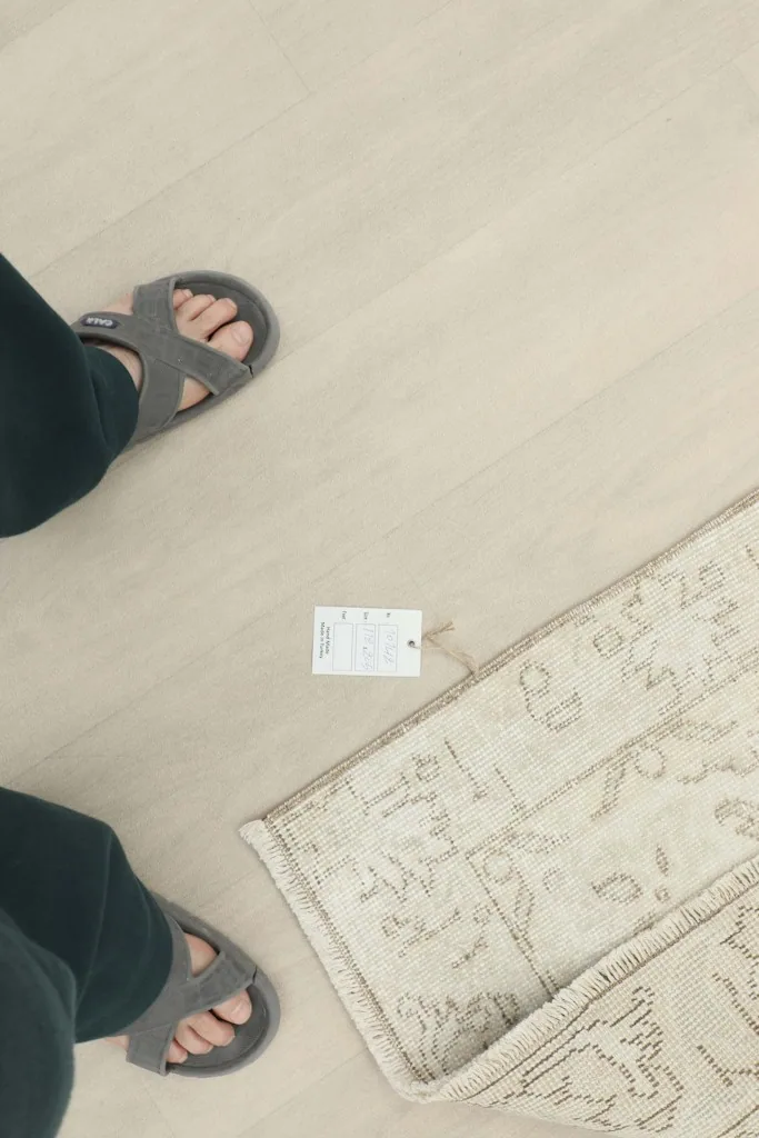 Overhead shot showing a foot in sandals next to the rug and its product tag for scale.
