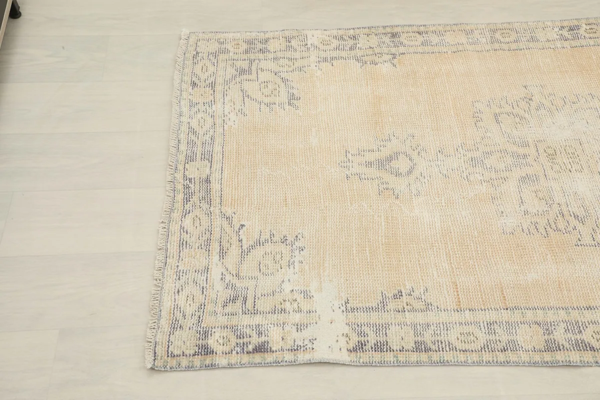 Close-up of the upper left corner of the beige rug, highlighting the faded gray motifs and natural wear