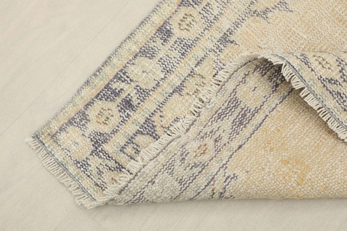 Corner of the rug folded back, revealing the cotton foundation and the reverse side of the hand-knotting
