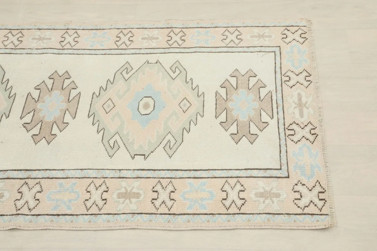 Close-up of the rug's corner, highlighting the ivory field, blue and tan geometric motifs, and border