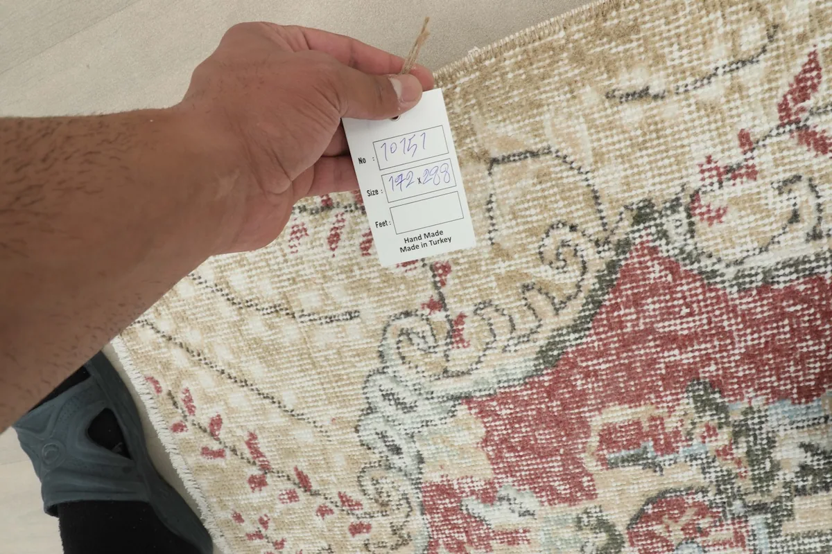 Hand holding a tag showing the rug's details, including its hand-knotted origin in Turkey.