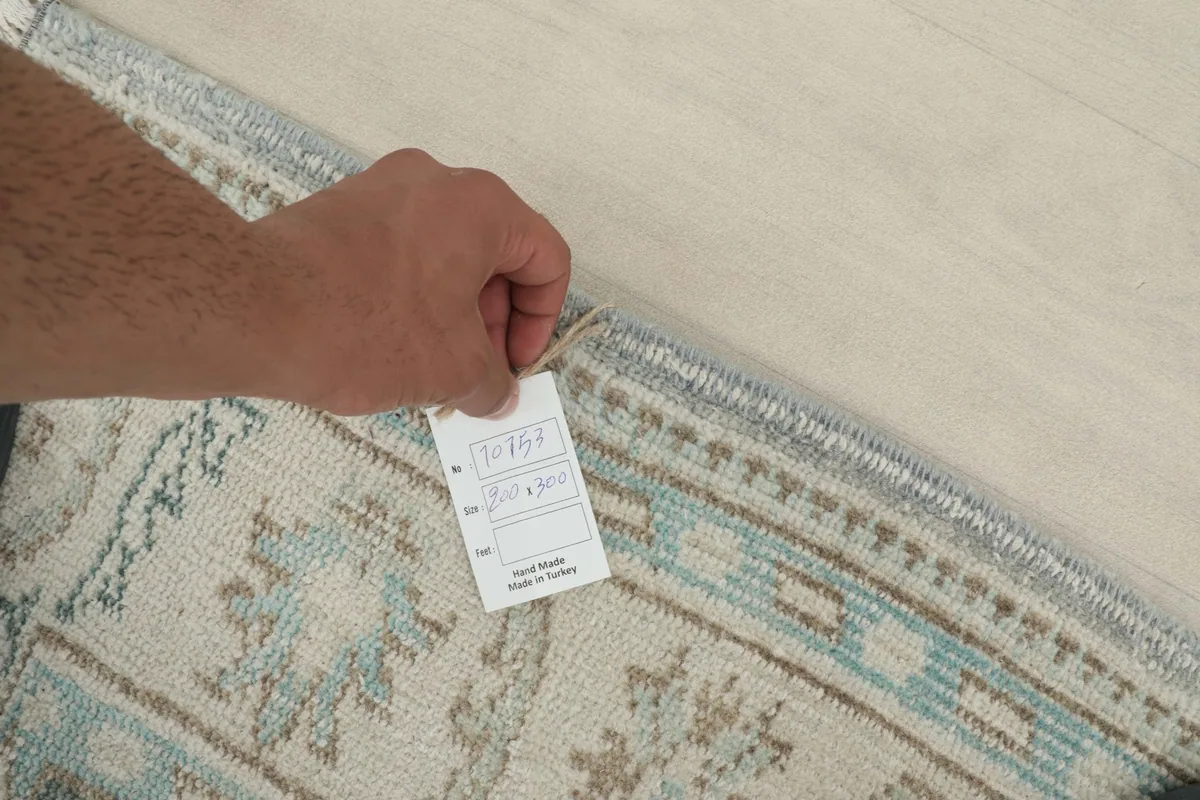 Hand holding a tag on the back of the rug, indicating its origin and material