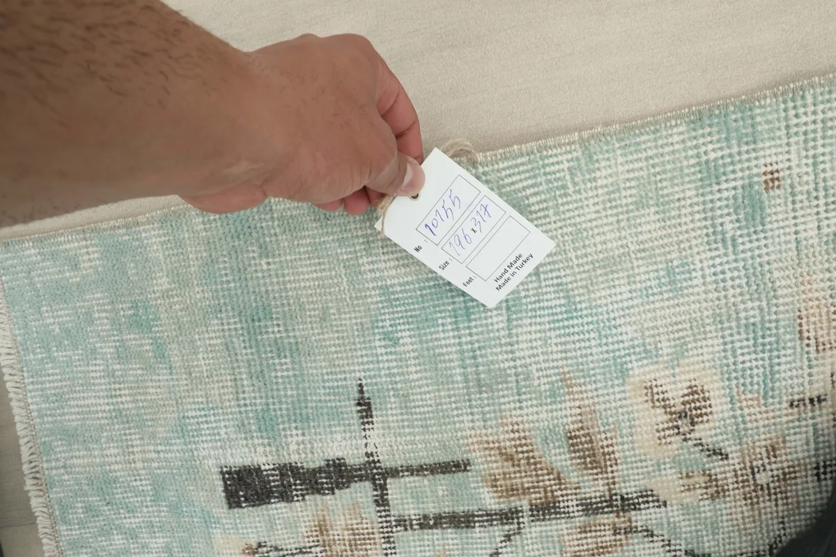Hand holding a tag near the rug, showing the texture and pattern details.
