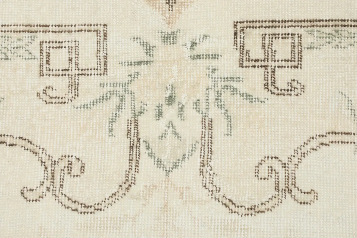 Detailed view of the intricate, faded gray and olive motifs on the ivory field