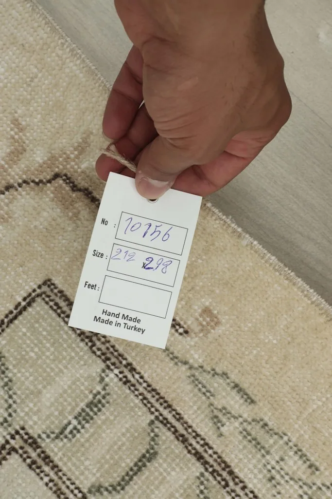 Hand holding a tag with the rug's dimensions (212x298 cm) and 'Hand Made in Turkey'